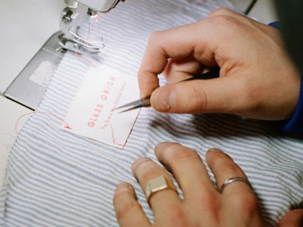 Close up of hand stitching Glass Onion label into a shirt